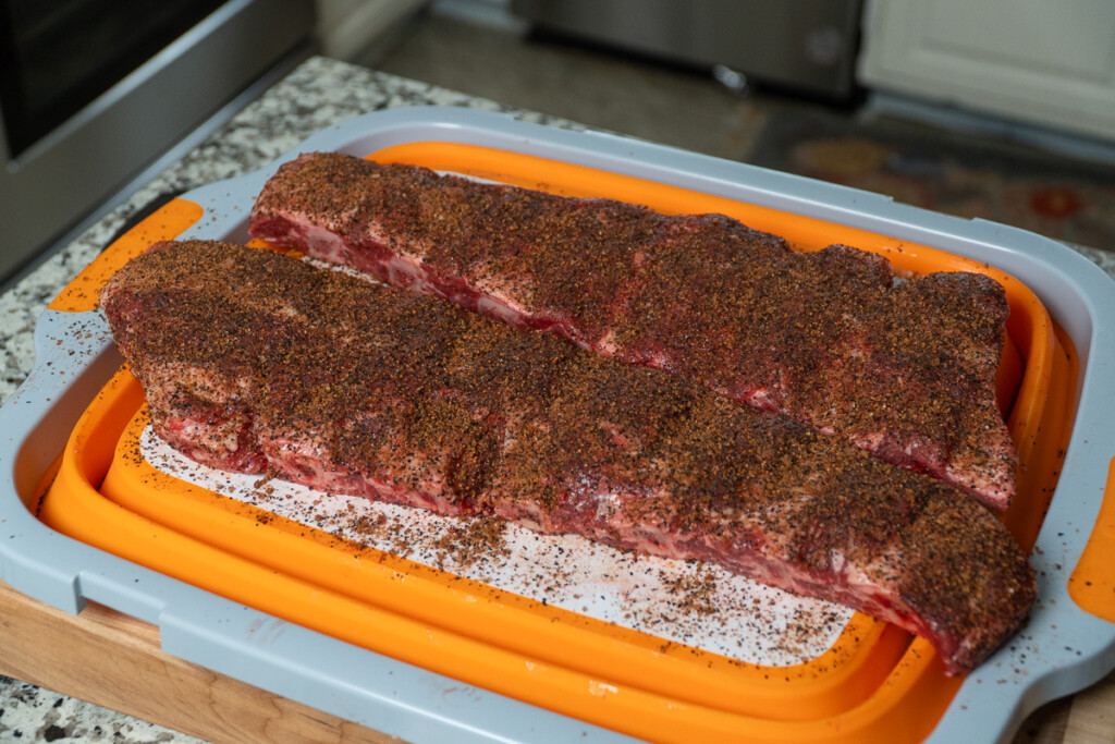 two slabs of raw beef back ribs seasoned on a white and orange board