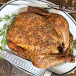 Whole smoked chicken with crispy, seasoned skin, served on a platter with fresh rosemary and carving knives.