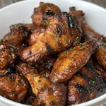Smoked chicken wings with a caramelized, crispy exterior, coated in sauce and served in a white bowl.