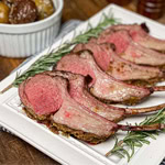 Sliced smoked rack of lamb served on a white platter with rosemary garnish.