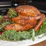Whole smoked turkey with golden-brown, crispy skin, garnished with fresh herbs on a serving platter.