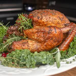 Whole smoked turkey with crispy golden skin, garnished with fresh herbs on a white platter.