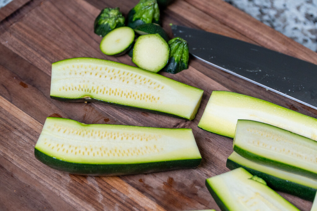 raw zucchini cut in half on a wooden board with a knife in the background