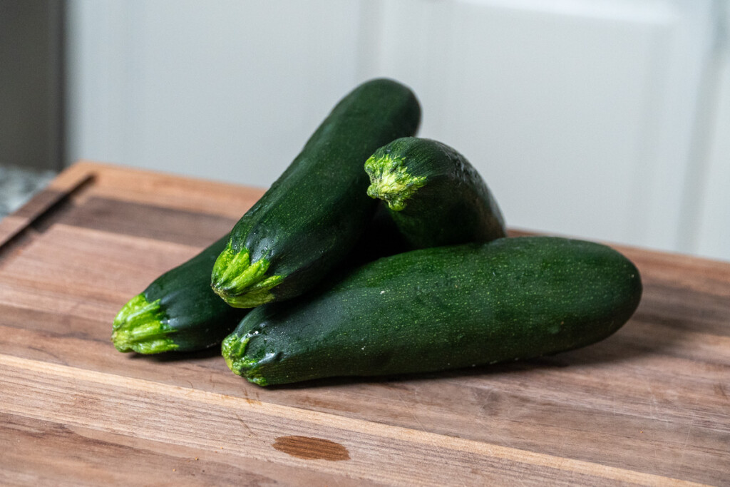 four raw zucchini on a wooden chopping board