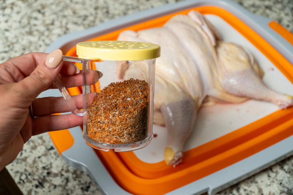 smoked chicken rub in a jar being held by a hand with a raw chicken in the background