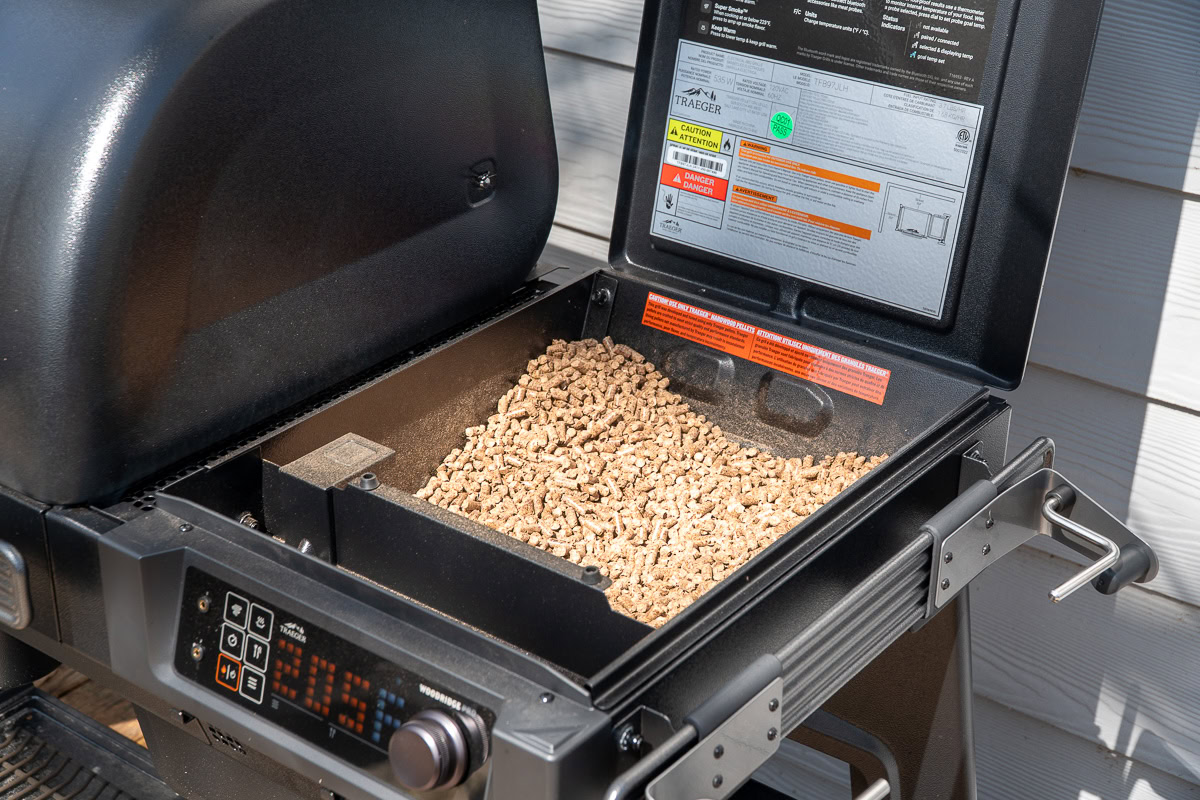 Open hopper on the Traeger Woodridge Pro filled with wood pellets and internal safety labels visible.
