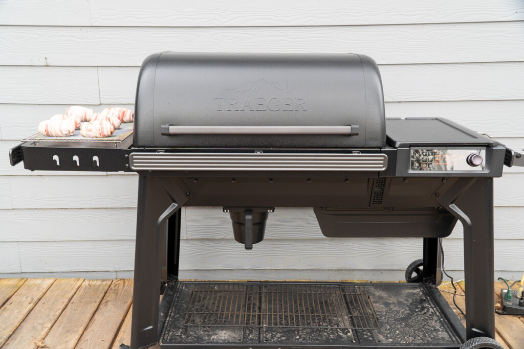 Full grill setup showing the Woodridge Pro in use with food staged on the side shelf and storage hooks visible.