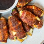 Bacon-wrapped jalapeño poppers stuffed with cheese, served on a white plate with barbecue sauce