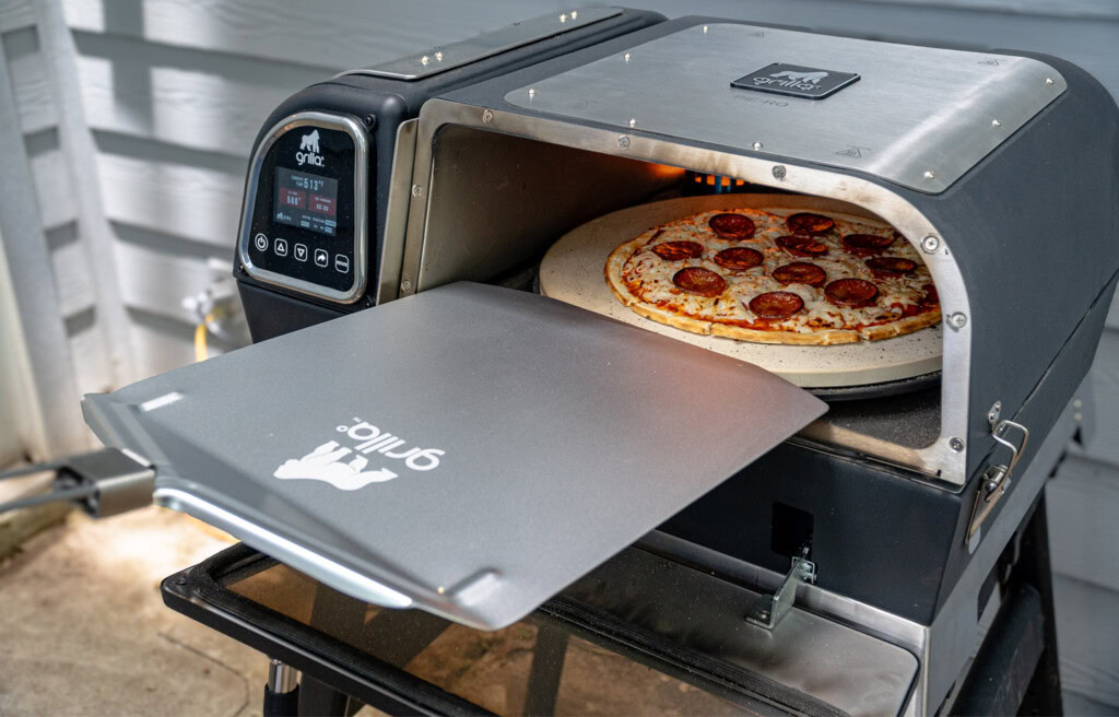 Grilla pizza oven with a freshly baked pepperoni pizza being pulled out, showcasing the oven's temperature display and sleek design