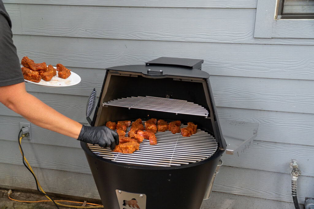 a person with black gloves is placing raw party ribs on the grill