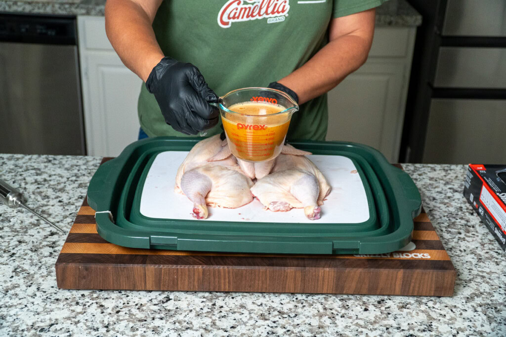 a person holding a jug of injection over a raw halved chicken