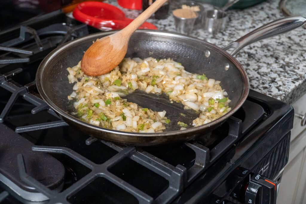 onion and jalapeno cooked down in a frypan being stirred with a wooden spoon