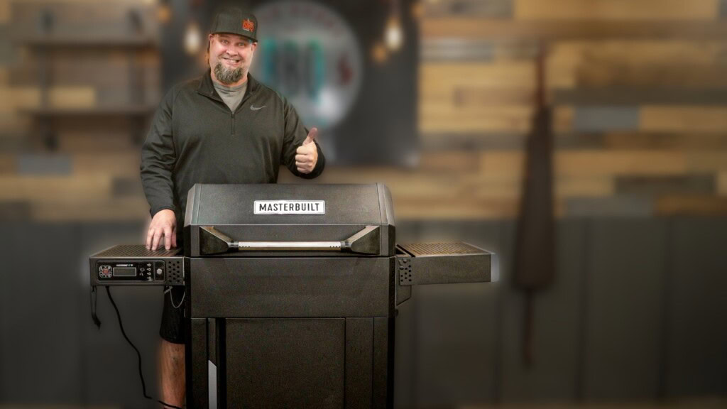 Man giving a thumbs up while standing behind a Masterbuilt AutoIgnite 545 gravity-fed charcoal grill during a review video setup.