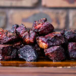 Smoked poor man’s burnt ends made from beef chuck roast, stacked on a wooden board with a dark bark and juicy interior.
