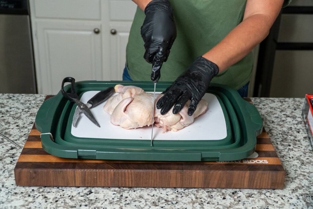 a person cutting a line down the middle of a raw chickens breastbone