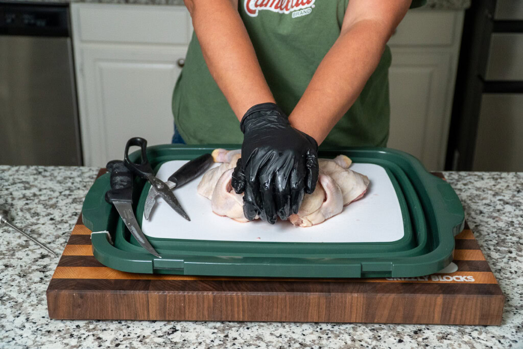 a person putting pressure on the raw spatchcocked chicken to flatten it out