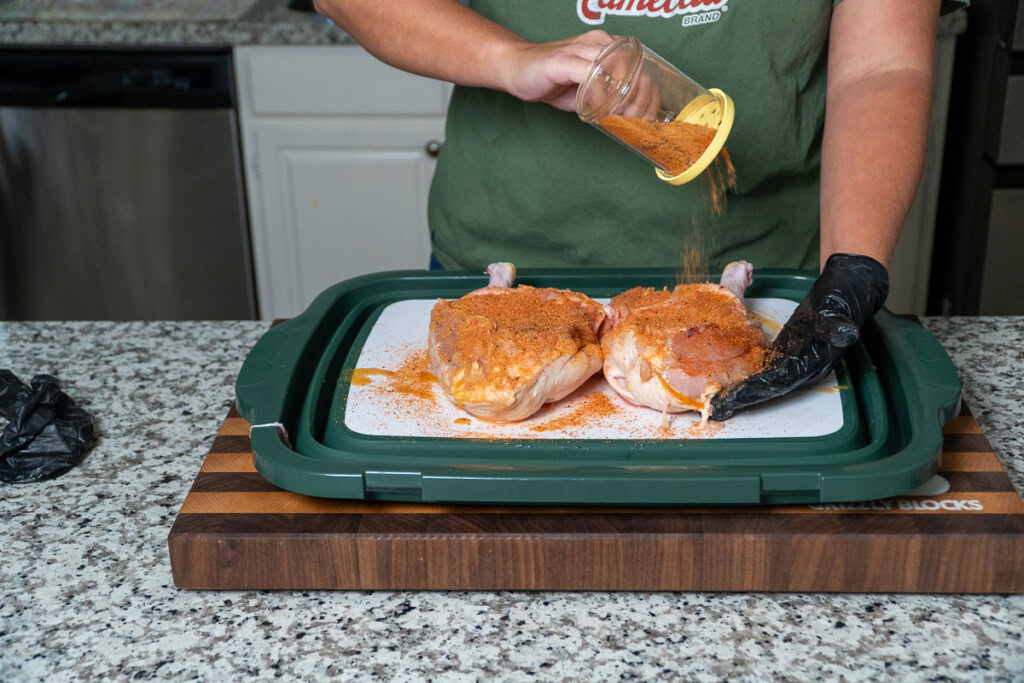 a seasoned raw chicken halved being sprinkled with seasoning
