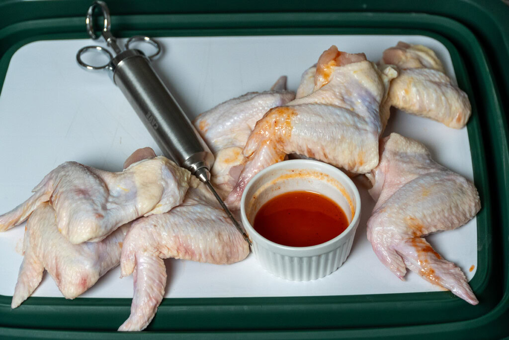 a plate with raw wings, bowl of hoy sauce, an injector