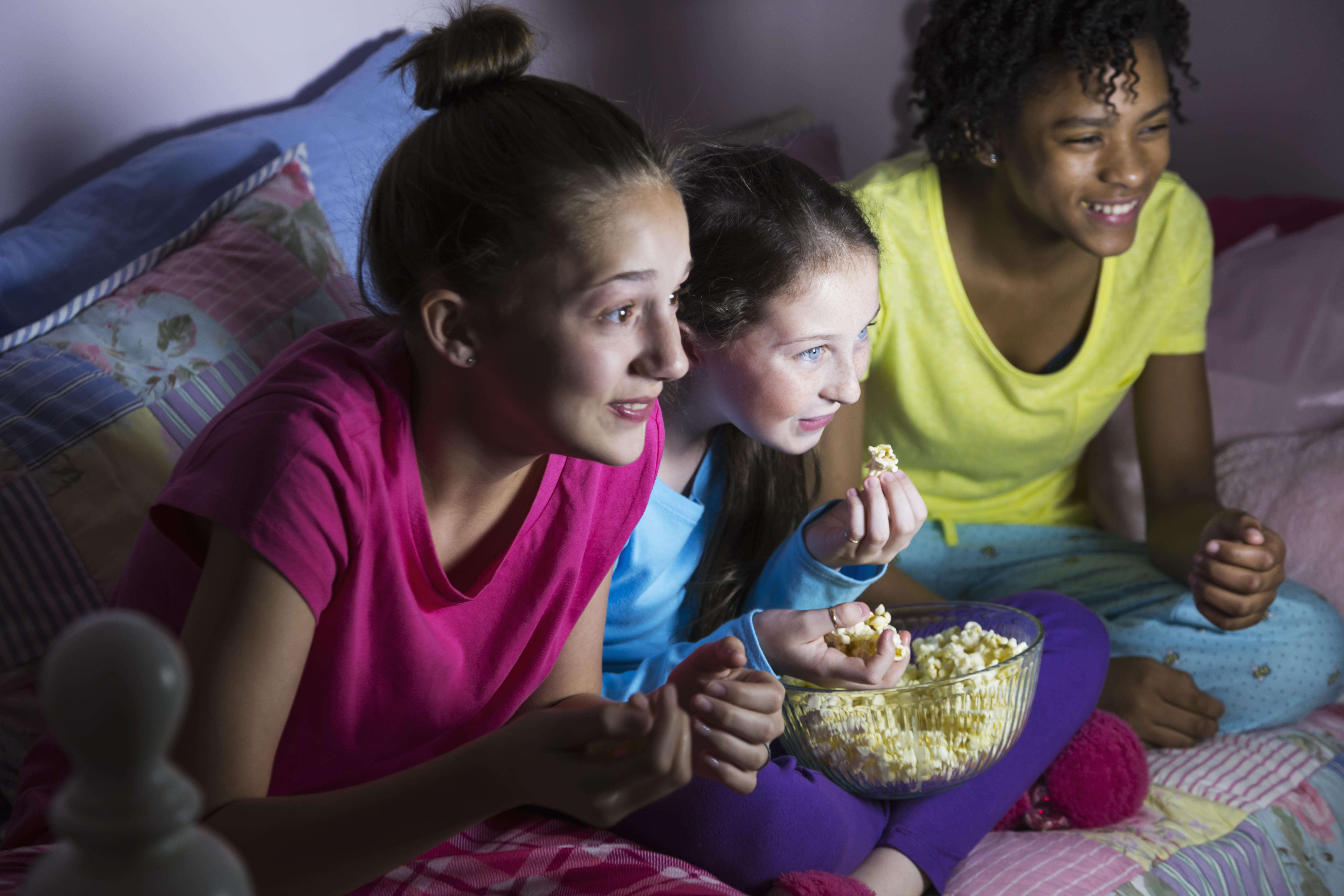 Preteen girls at sleepover watching tv, eating popcorn