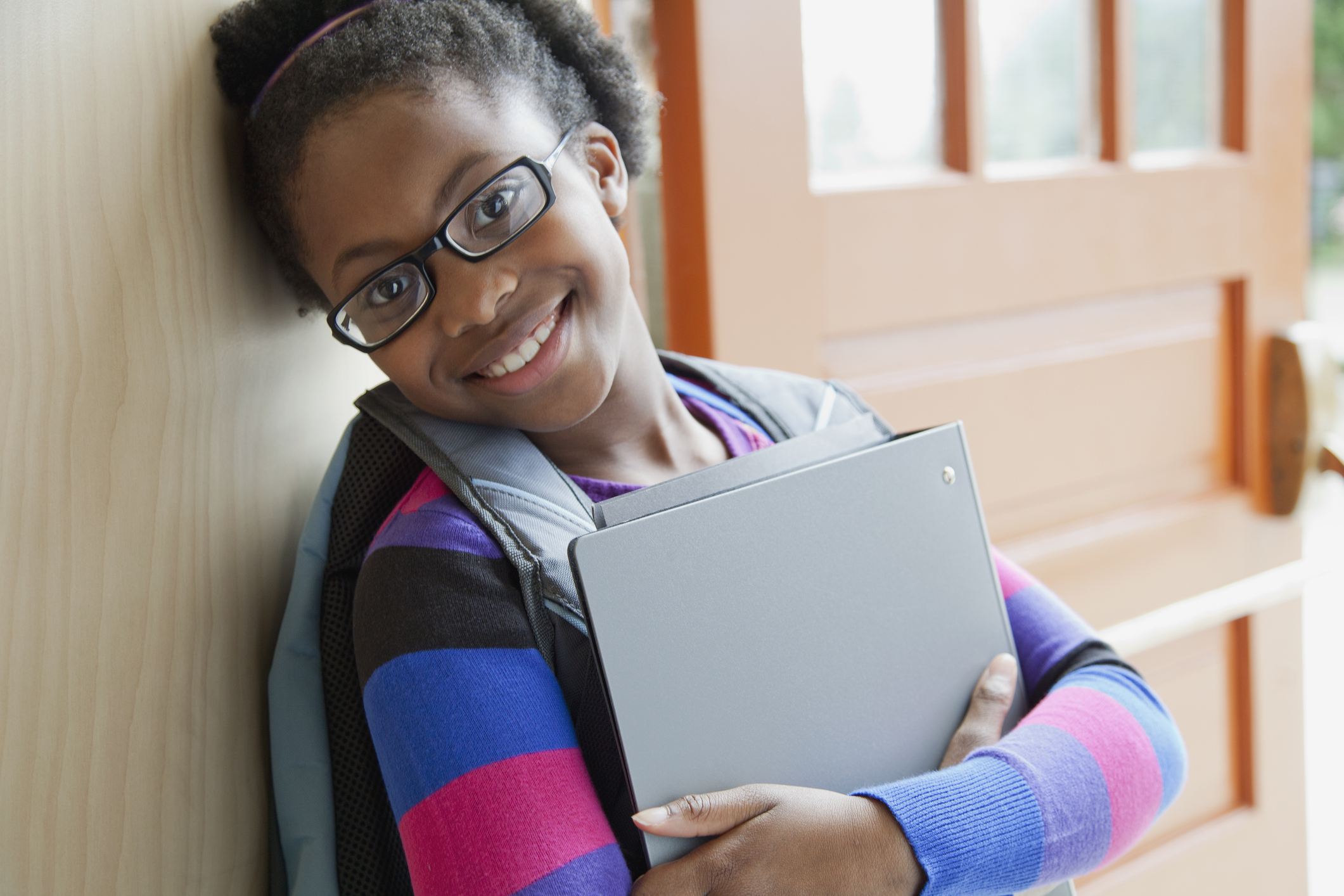 African American elementary student holding books at doorway.