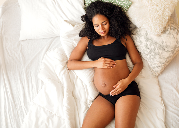 High Angle View Of Pregnant Woman Lying On Bed