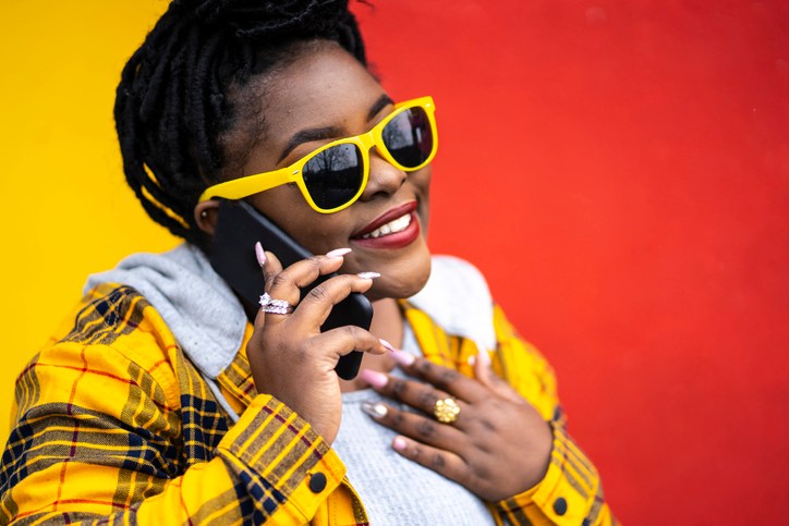 Young woman standing on colored background and talking on phone