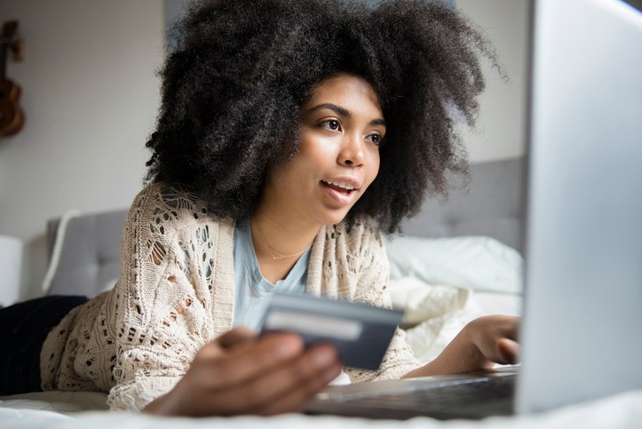 African American woman laying in bed online shopping with laptop