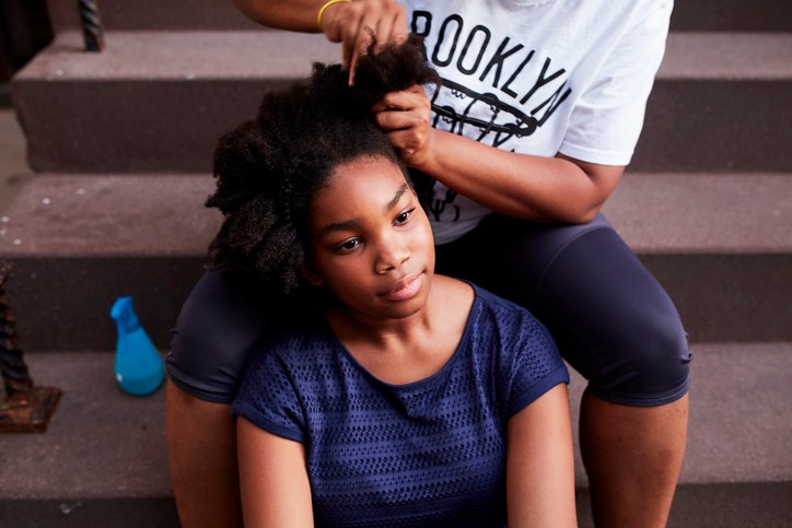 Black mother styling hair of daughter on staircase