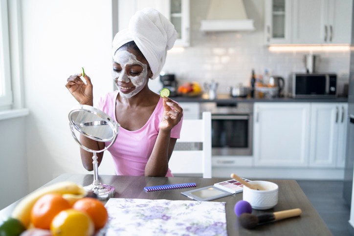 Smiling african woman with facial mask and towel on head, at home
