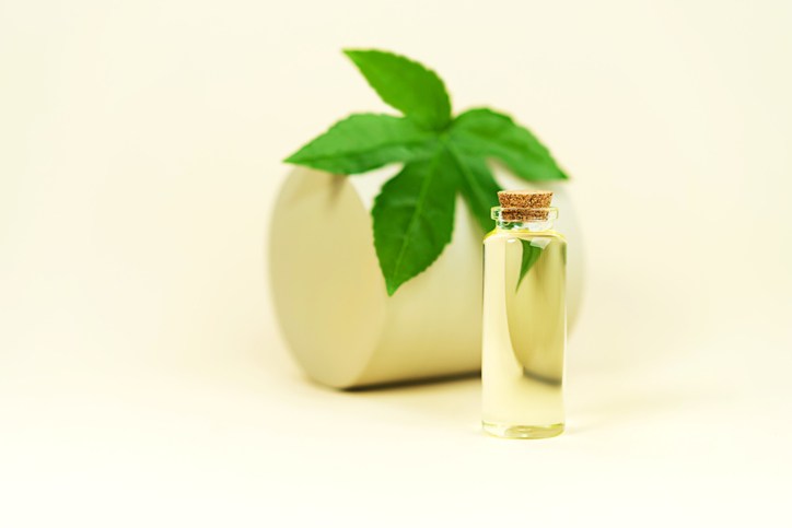 Glass bottle with herbal CBD oil, THC tincture and hemp leaf on pastel beige background.