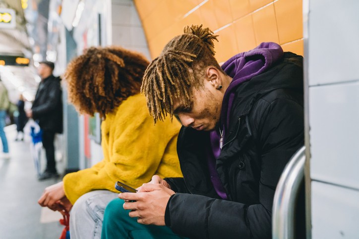 Young man playing with a smartphone while he's waiting for the subway train