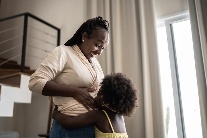 Girl kissing her pregnant mother's belly at home