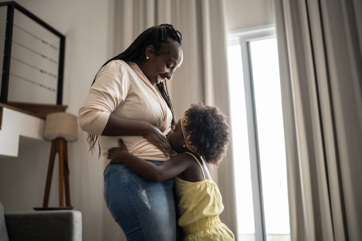 Girl kissing her pregnant mother's belly at home