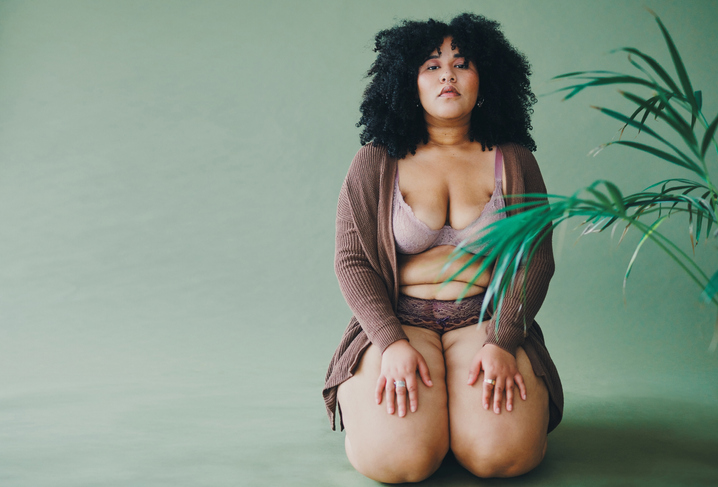 Full length portrait of an attractive and voluptuous young woman posing in her lingerie against a green background in studio