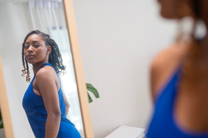 Create Your Own Style to Personality Development Make You More Attractive. A female African American in a tank top takes a look into a mirror and twists her body shape as she examines her reflection in a bedroom.