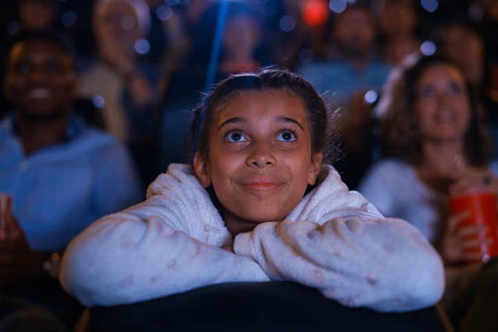 Mid-shot of young girl watching a film inside movie theater
