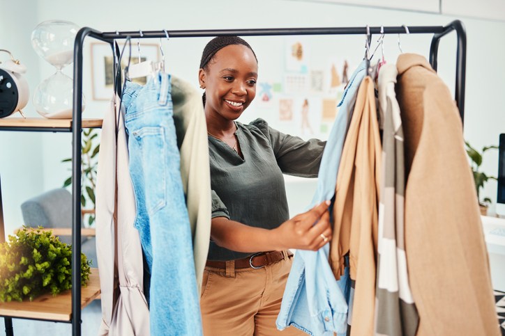 Customer, shopping and clothes rail with fashion, retail and choice for wardrobe, service and discount deal. Black woman client in shop for designer brand, happiness or product in luxury boutique