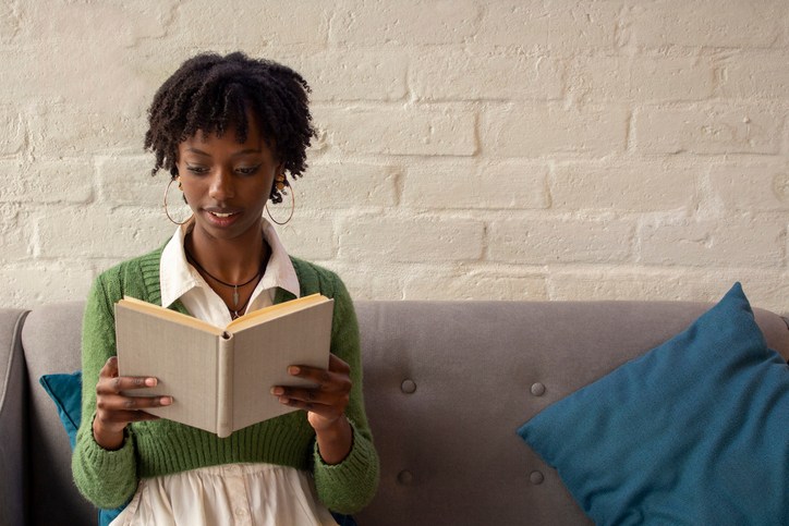 young african american woman sitting on a sofa reading a book attentively