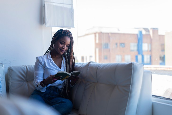 comfortably dressed Latin woman is inside her house sitting on the sofa in her living room reading a book