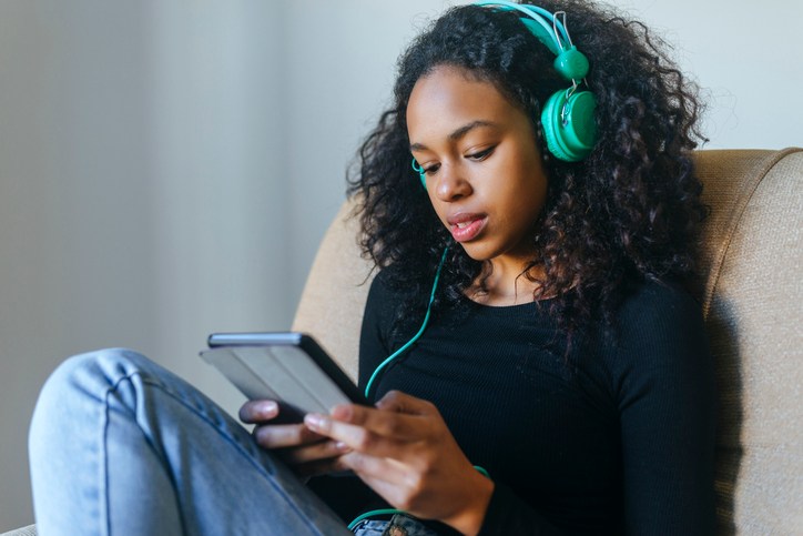 Portrait of young woman sitting in armchair listening music with headphones and tablet