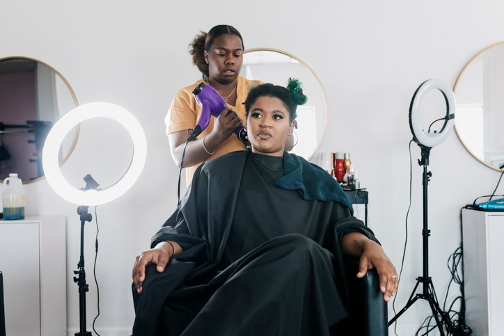 Black Woman Sitting In Chair Getting Hair Styled By Her Hairdresser