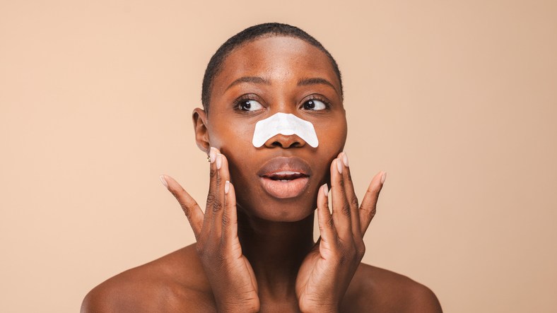 Black woman with short hair applies a nose strip, touching face.