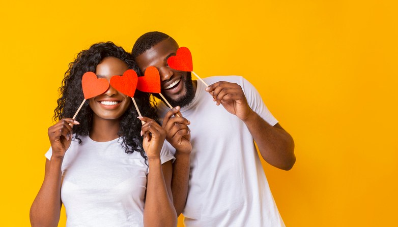 Young afro couple holding red love hearts over eyes