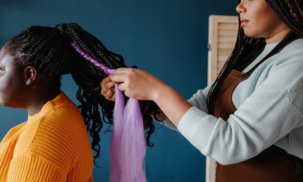 Close-up of confident hairdresser braiding hair to a young African woman in salon