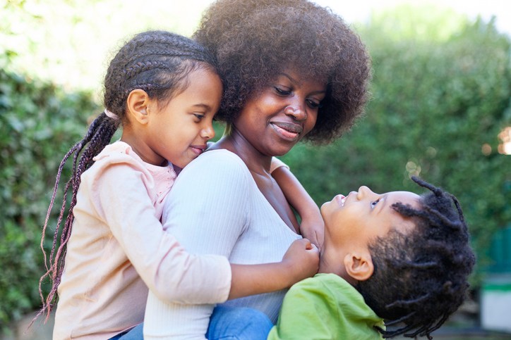 Happy African Mother Carrying Son And Daughter As They Play In Backyard