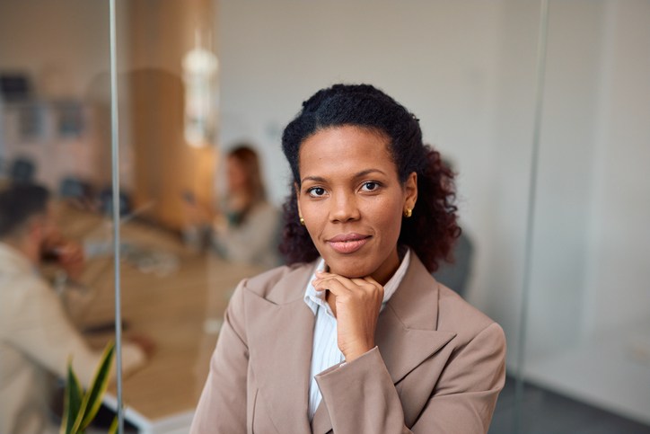 black women jobs, unemployment
Confident businesswoman posing in modern office with team working in background