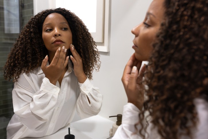 Young woman checking her skin in the bathroom mirror