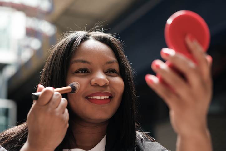 Businesswoman applying makeup with a brush and mirror