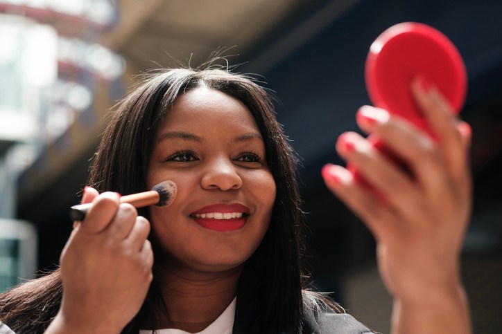 Businesswoman applying makeup with a brush and mirror, beauty products 