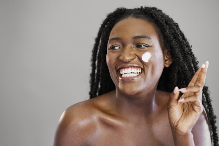 Happy Black Woman Laughing while Applying Skincare Face Cream